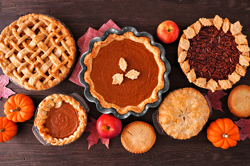 Assortment of homemade fall pies. Apple, pumpkin and pecan. Top down view table scene on a dark wood background.